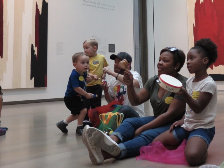 Kids and their parents play instruments in an art gallery