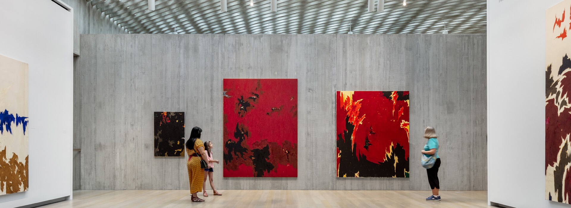 Woman and her daughter and another woman look at art in a large open art gallery at the Clyfford Still Museum