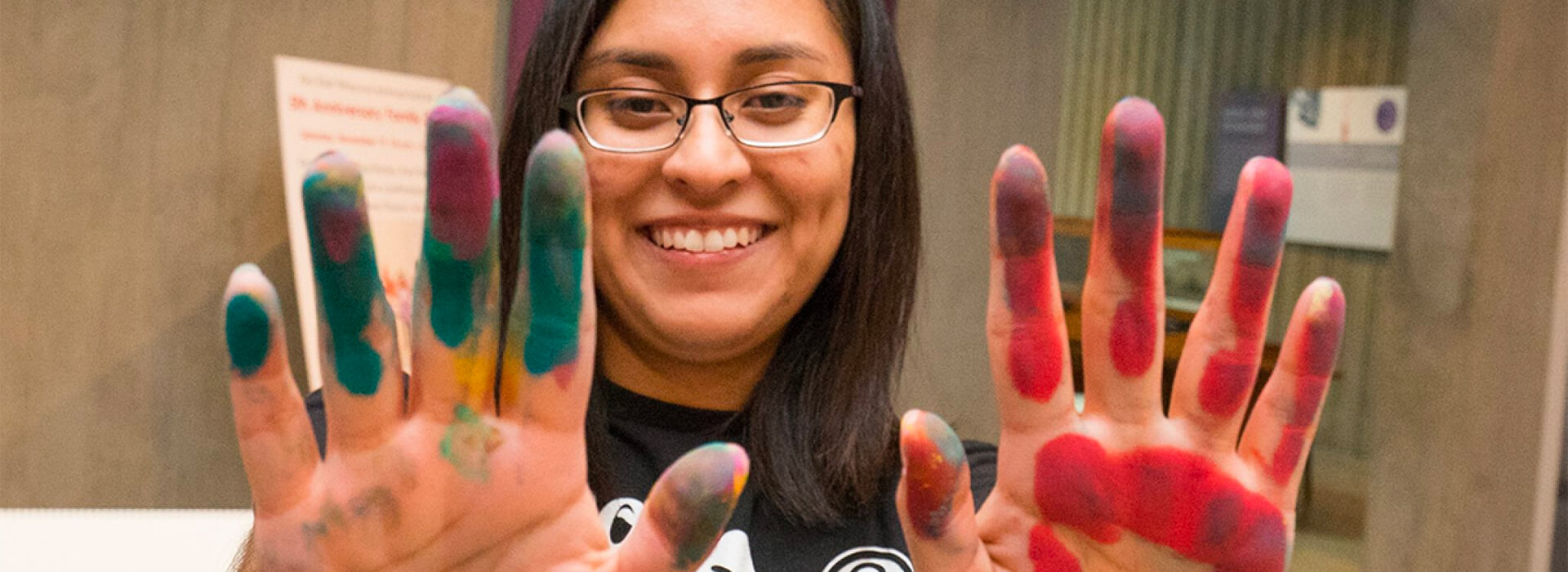 A woman holds up her hands with paint on them