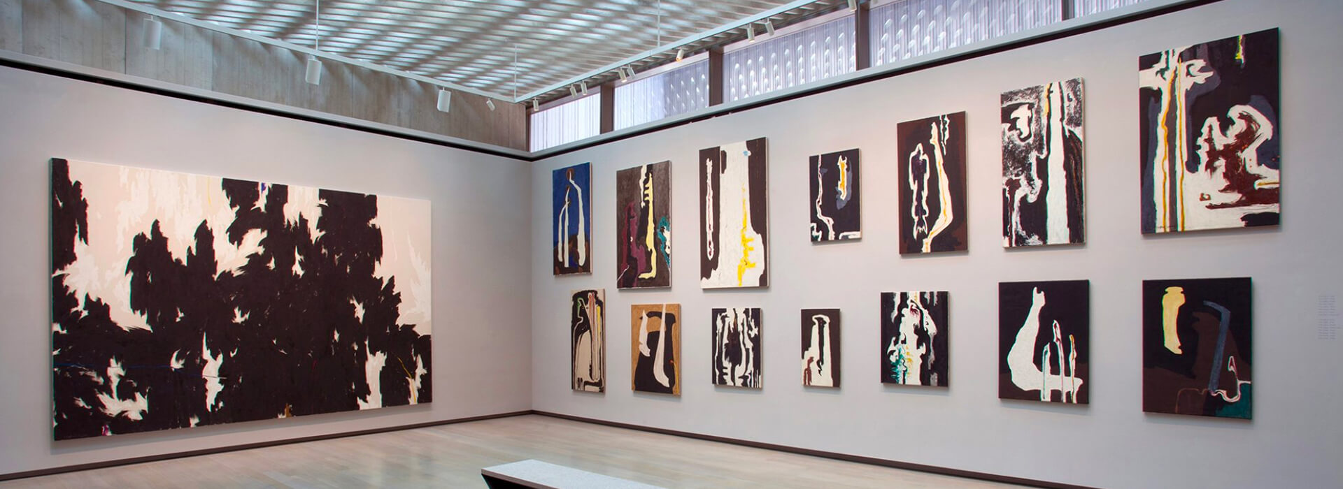 An empty gallery with one large abstract oil painting on one end and smaller pieces hanging on the adjacent wall