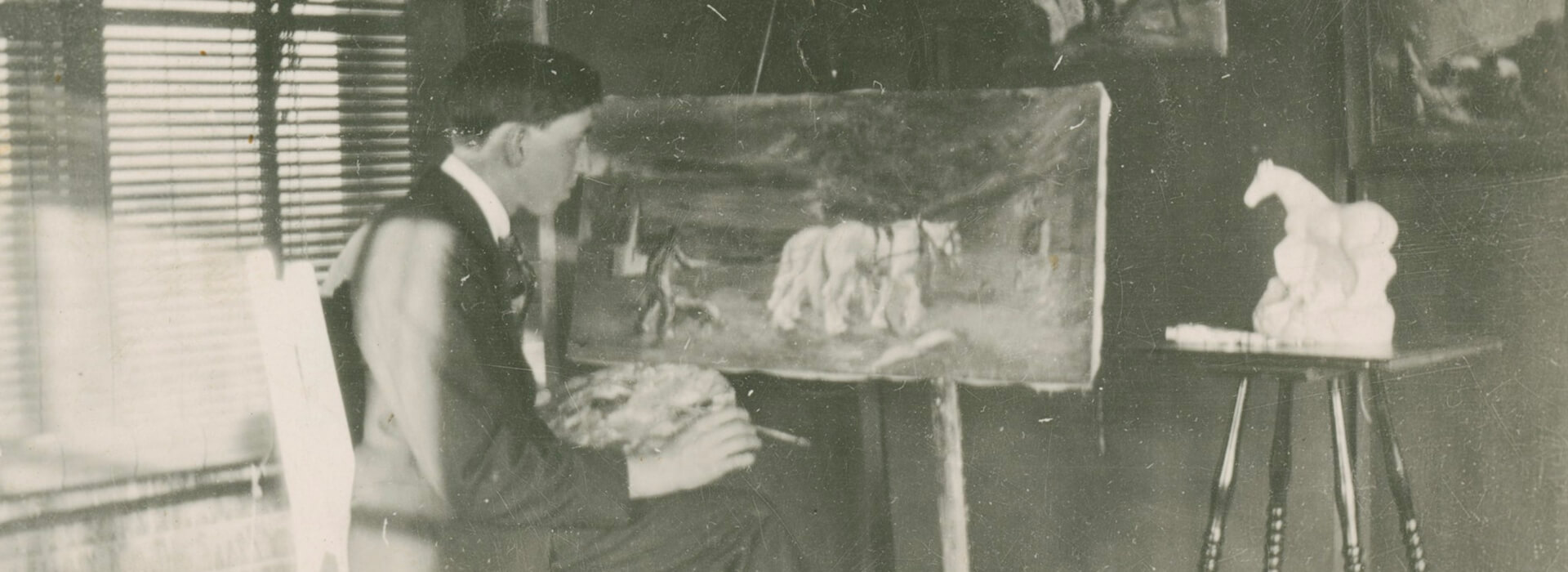 Black and white photo of a young Clyfford Still sitting down and painting a picture of horses