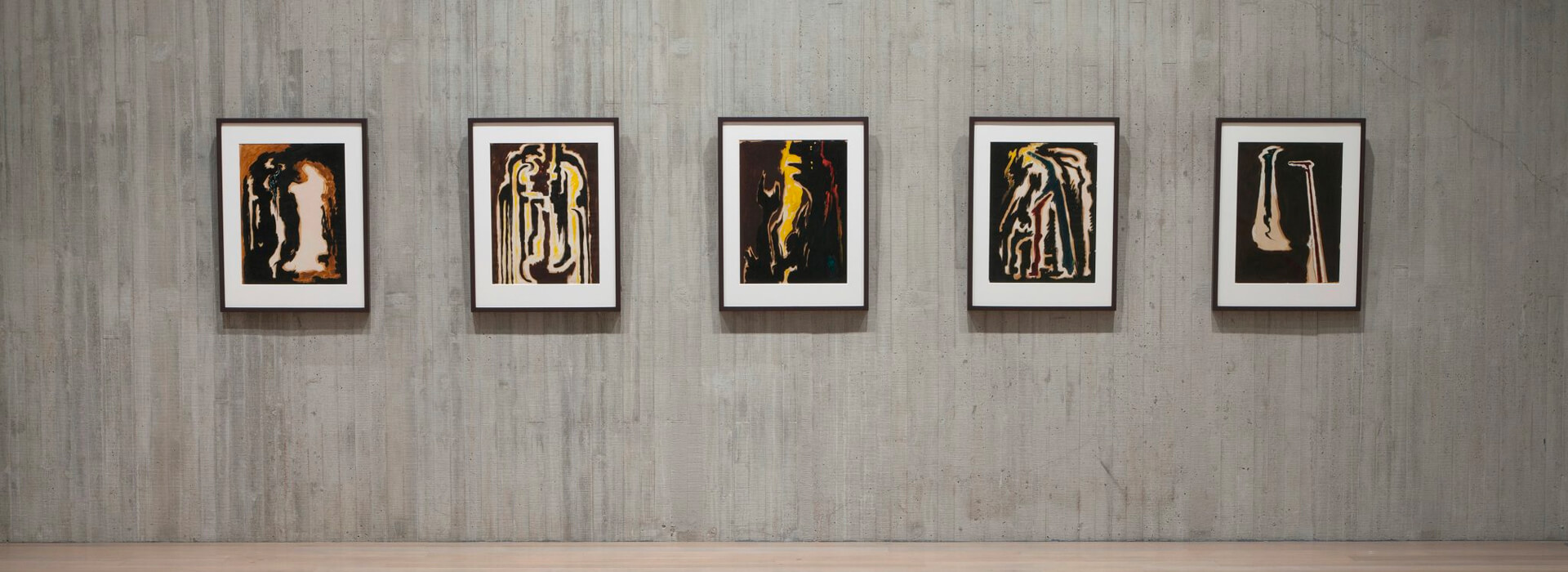 Framed abstract artworks on paper hang on a concrete wall