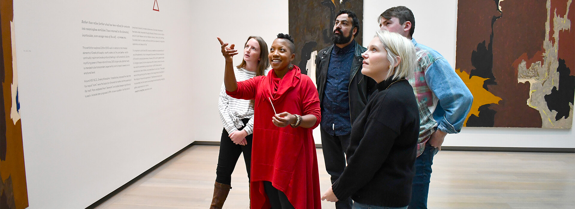 A group tours the Clyfford Still Museum and one participant points up while the others look at where she is pointing