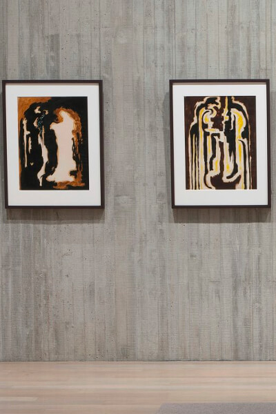 Two framed works on paper hang on a concrete wall