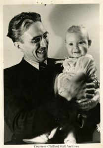 A photograph of Clyfford Still smiling holding his baby daugther