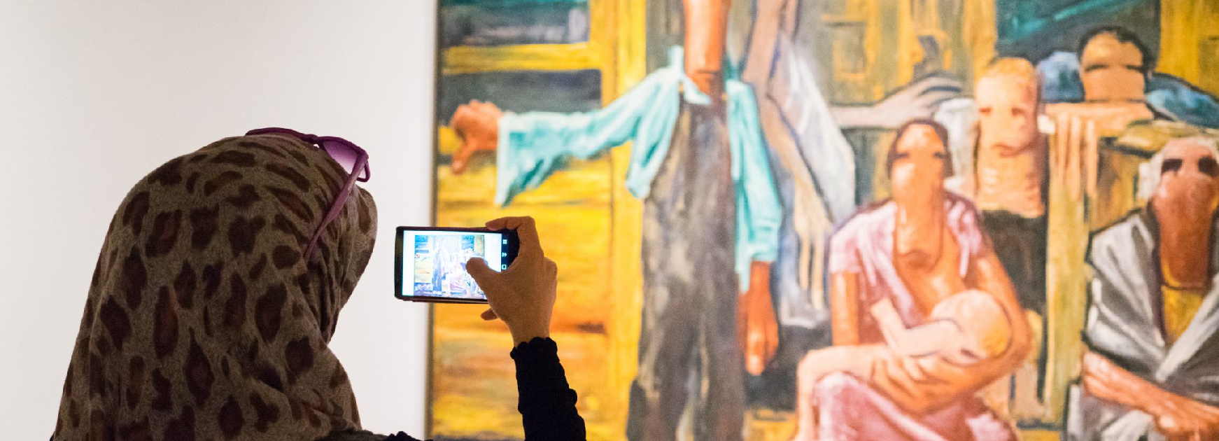 Woman wearing a leopard print scarf and sunglasses on her head holds her phone up to take a photo of an abstract painting of people by Clyfford Still