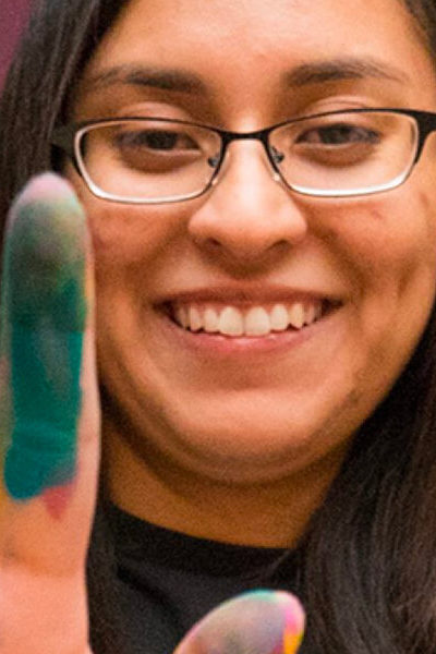 A young woman holds up her hands to the camera with paint on her fingers
