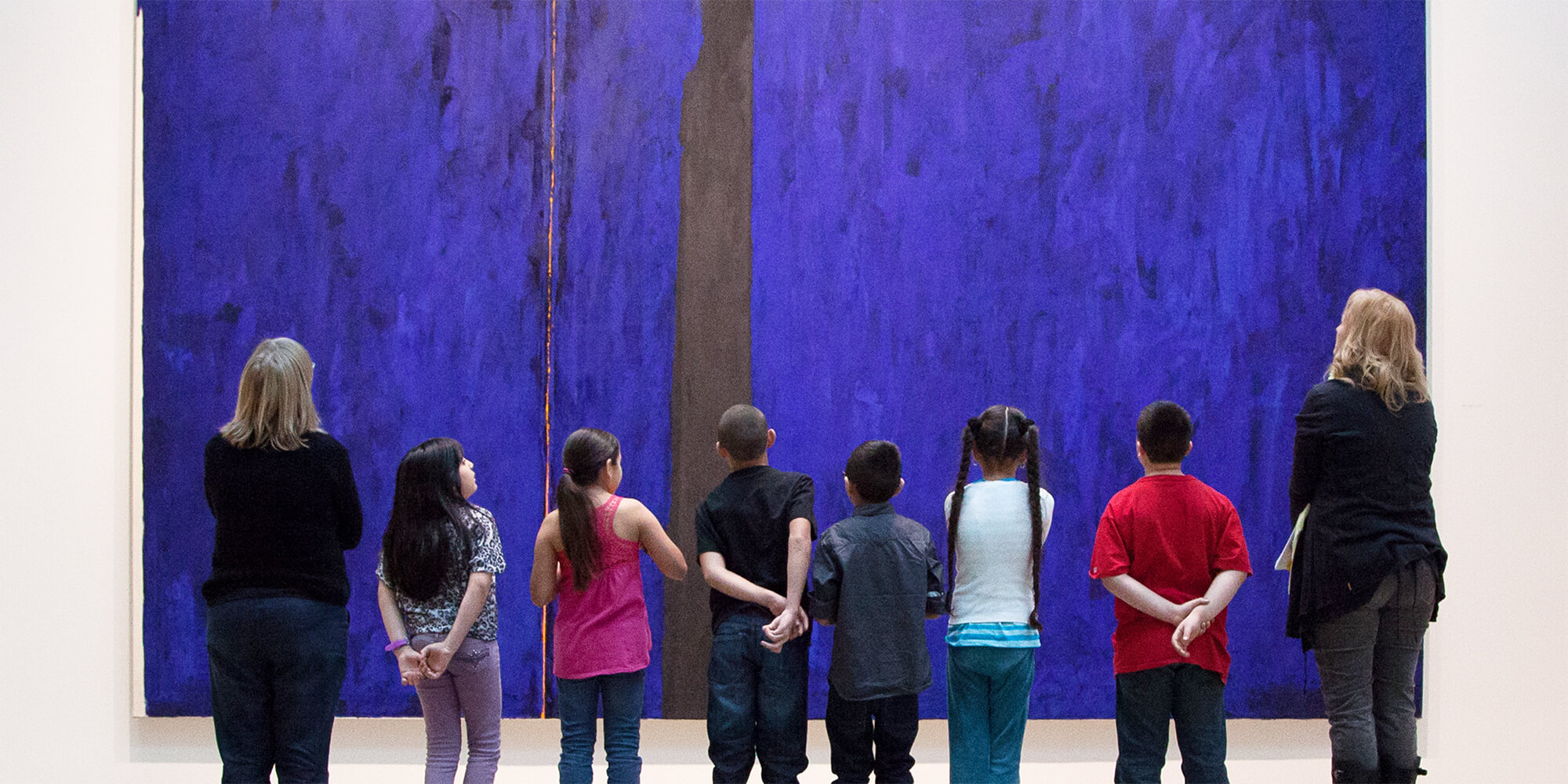 Children and teachers look up at a large blue painting