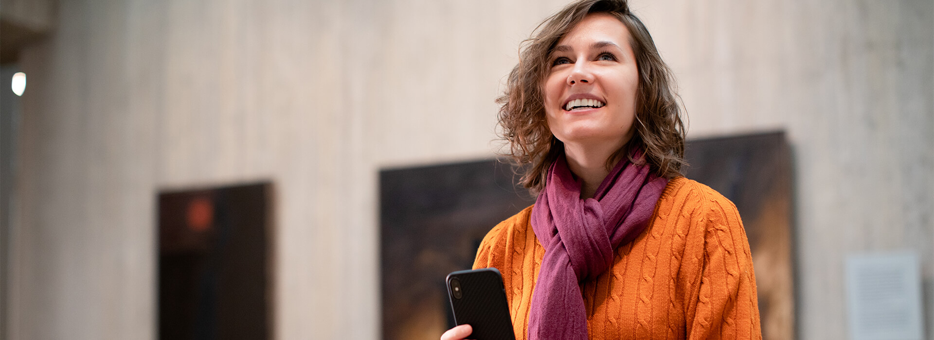 Woman holds a phone and smiles while looking up in a gallery