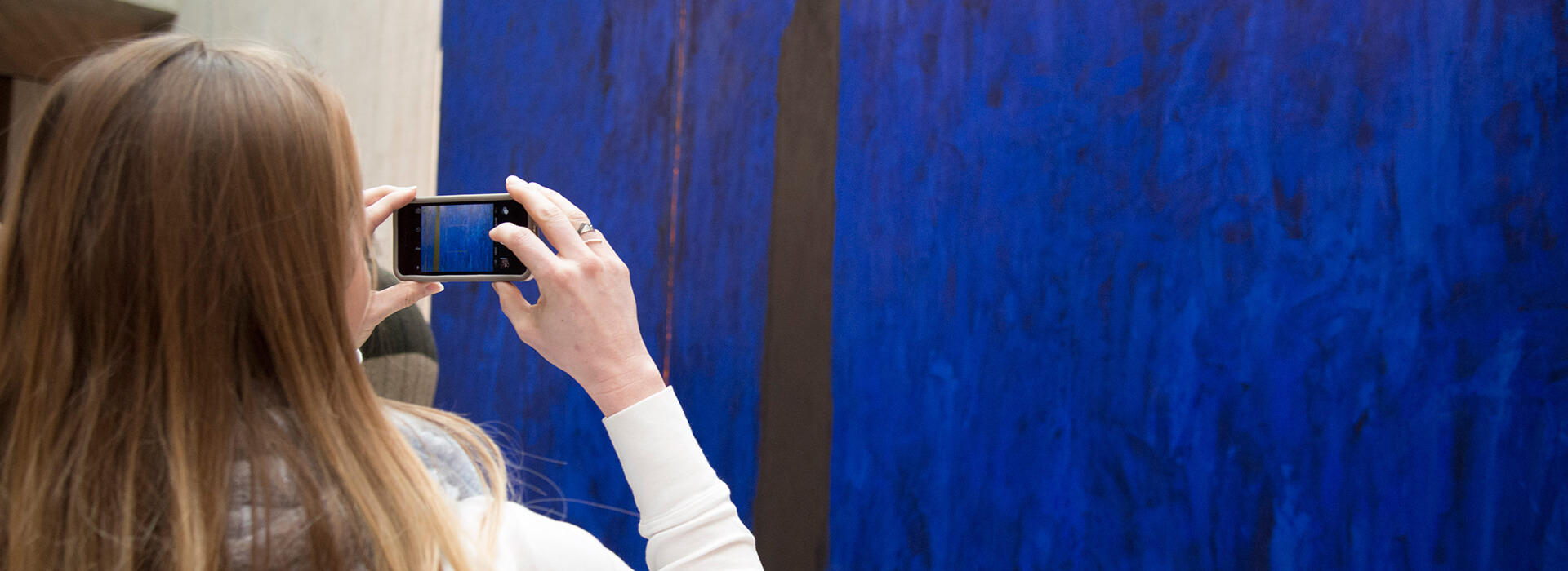 Woman takes a photo of a large blue painting with her phone