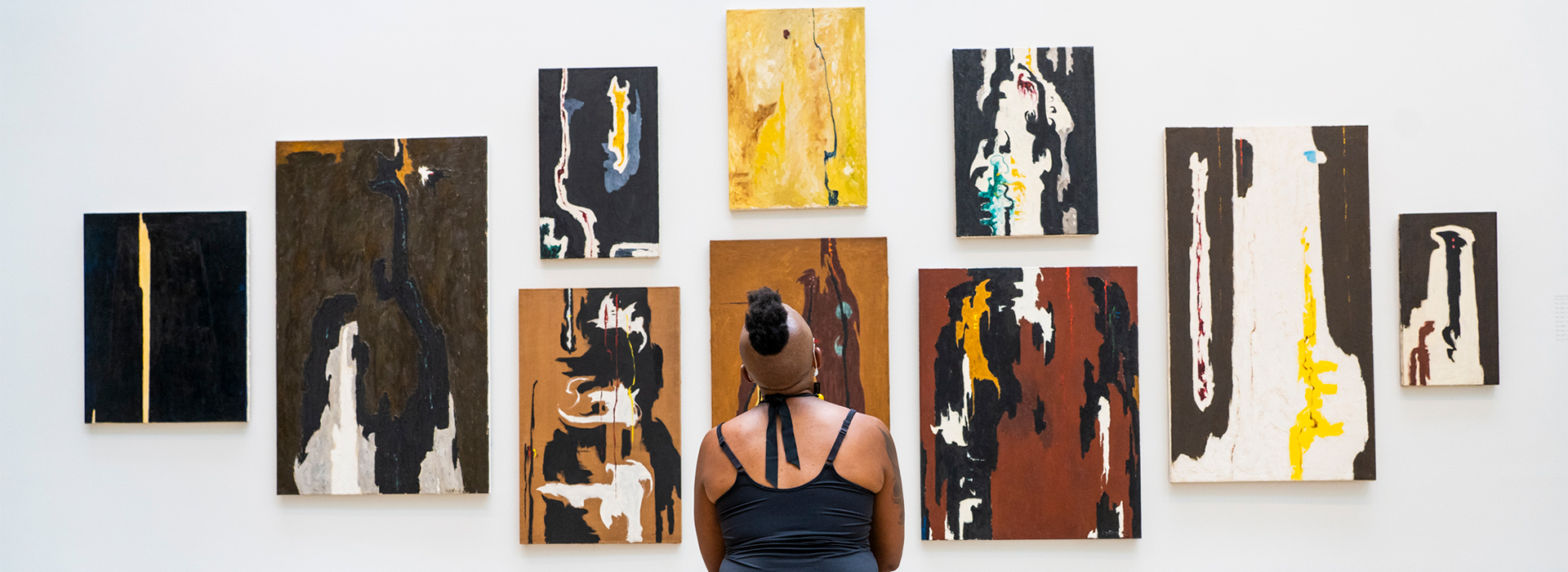 Woman looks up a a wall with many abstract oil paintings
