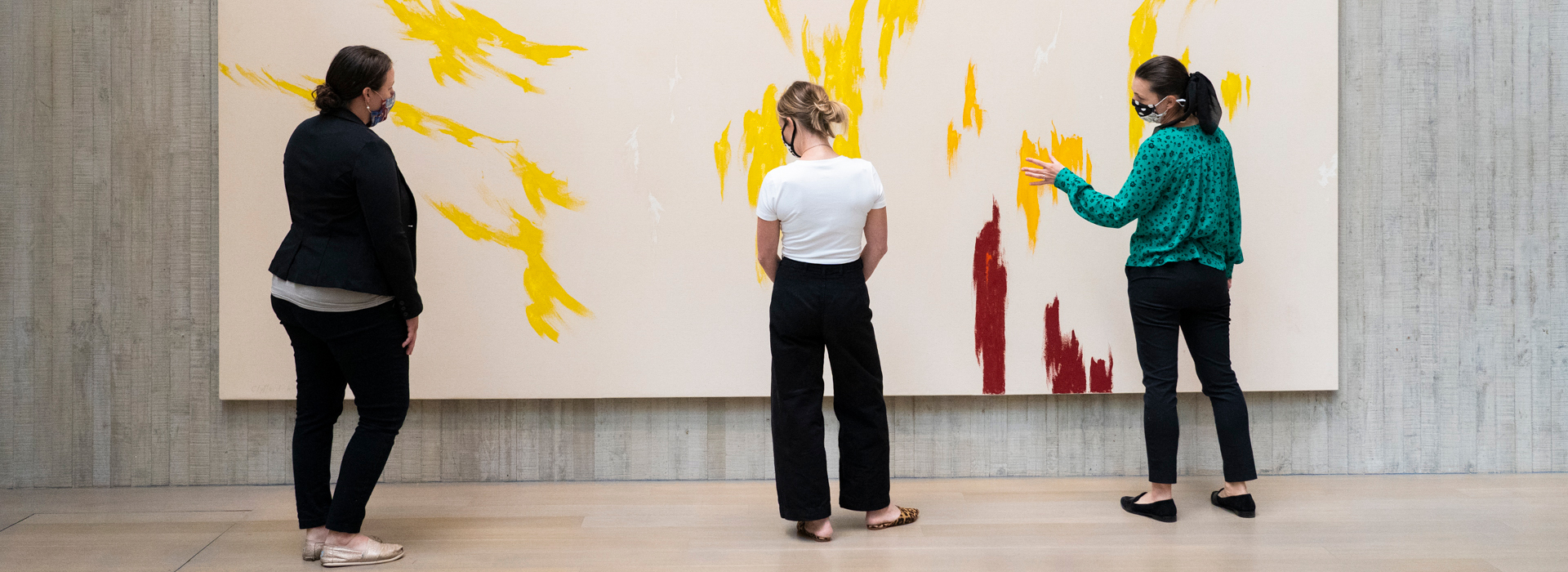 Three women look at a large abstract Clyfford Still painting while wearing masks