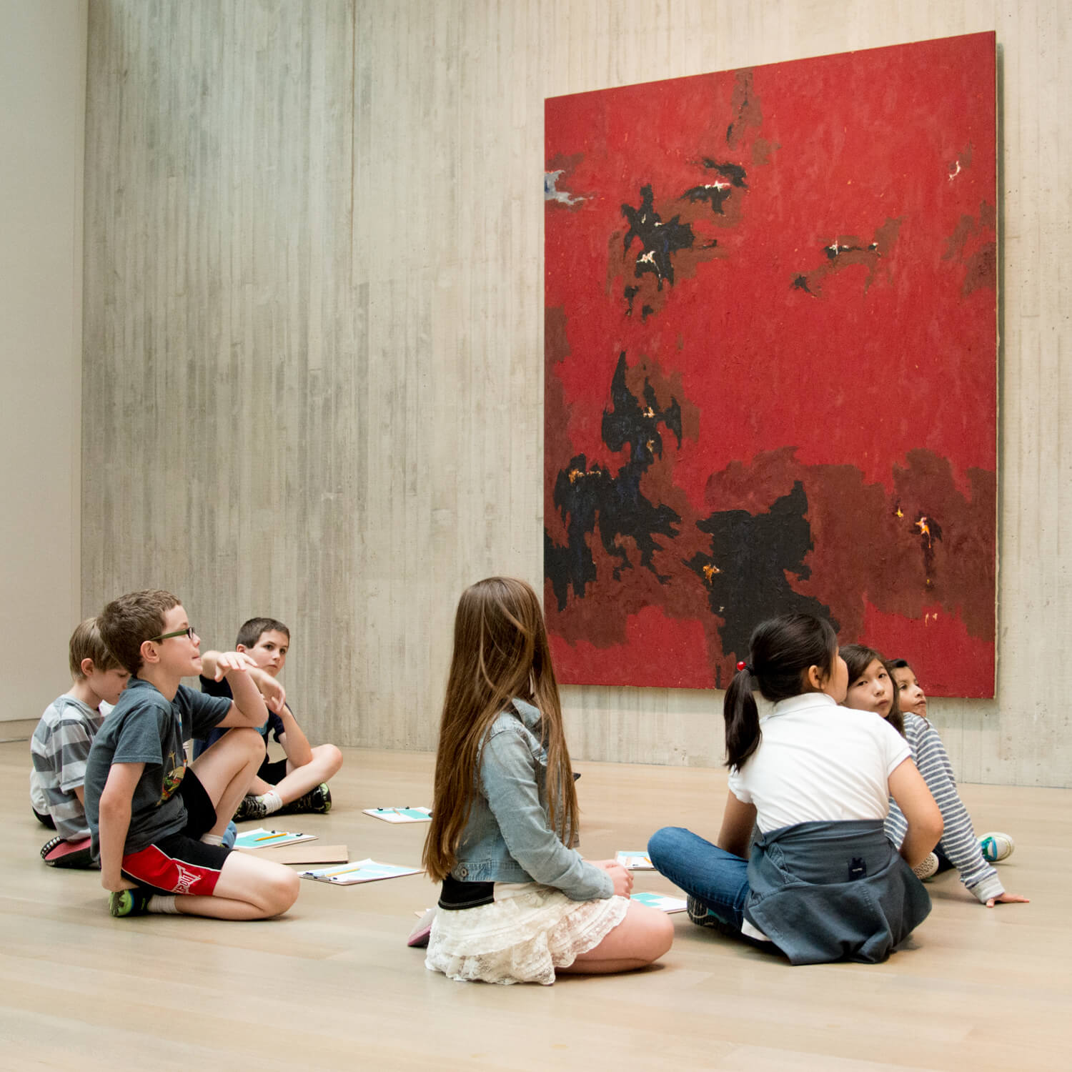 Students sit on the floor of a gallery looking up at the artwork