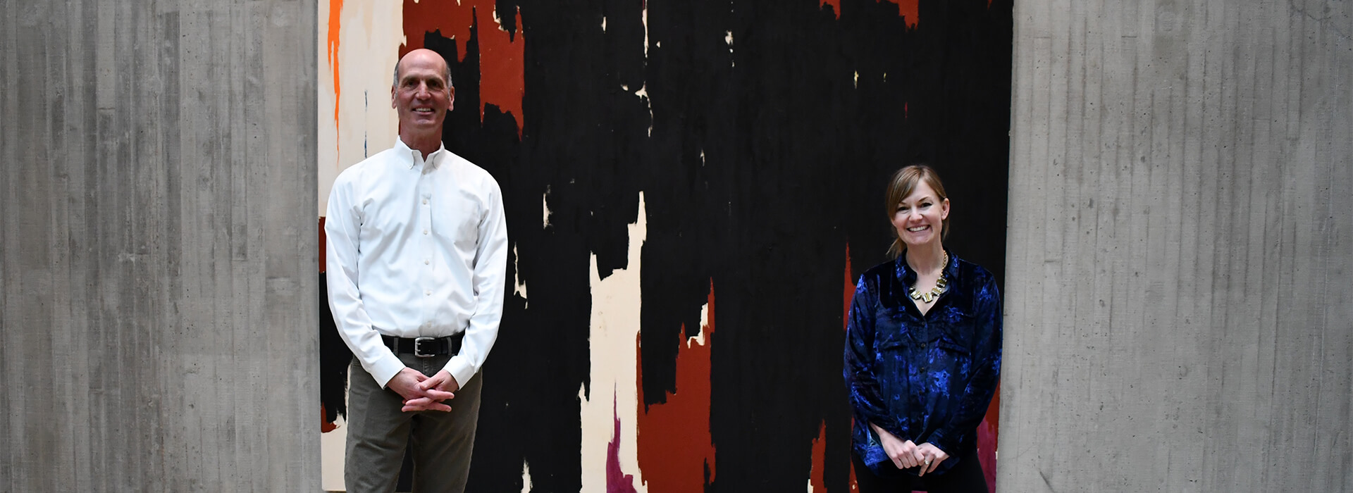 A man and woman stand in front of a large abstract black, red, white, and orange painting