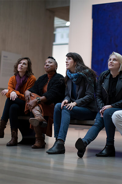 A group sits on a bench looking at art and talking about it