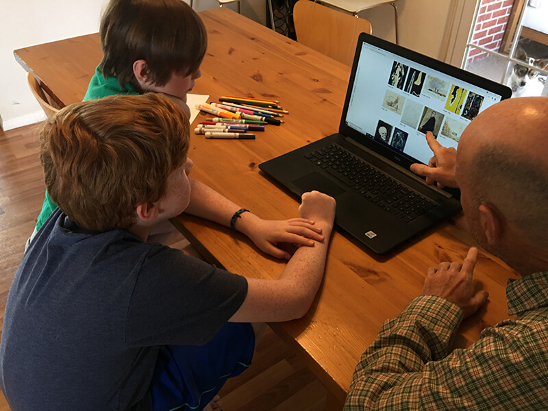 A father and his sons look at a laptop with an online collection of artwork