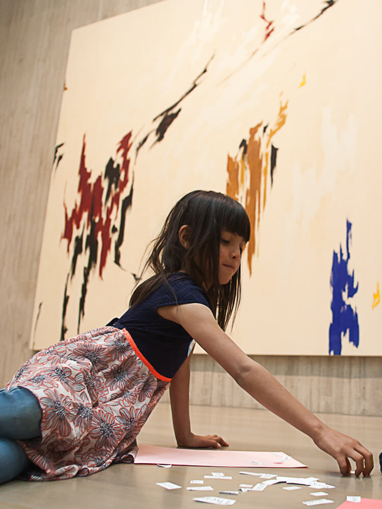 Young student sits on the floor in front of a painting with words on the floor