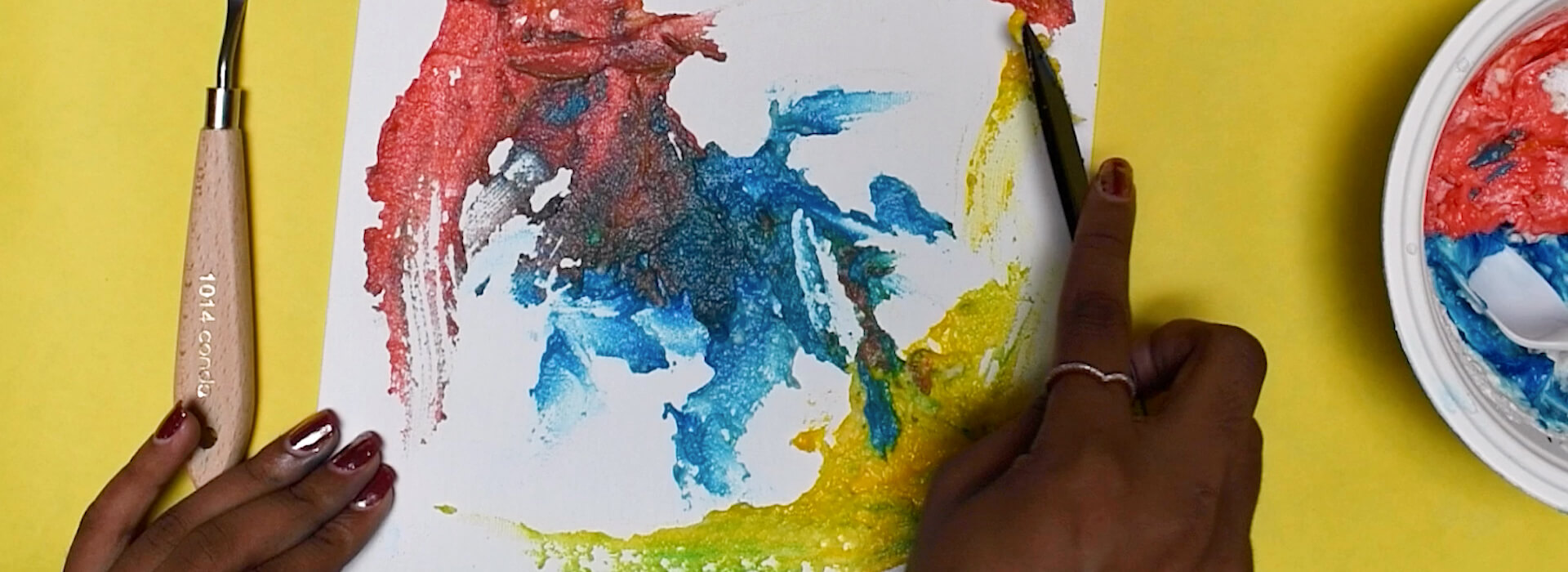 Looking down at a woman's hands as she uses a knife to paint paper with colorful paints
