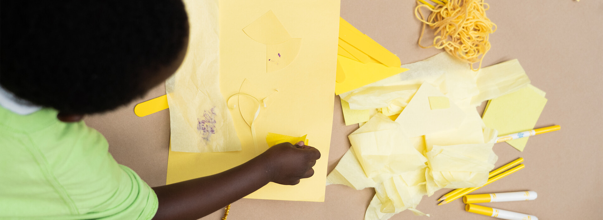 A child makes art with yellow paper and supplies