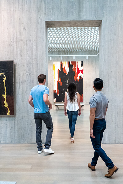 Two men and a woman walk through the concrete opening between two galleries at the Clyfford Still Museum