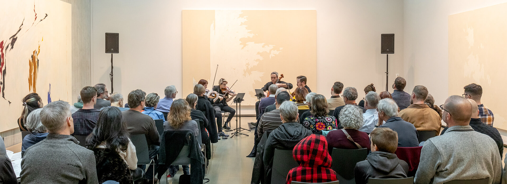 People seated in an art gallery watch a string quartet perform