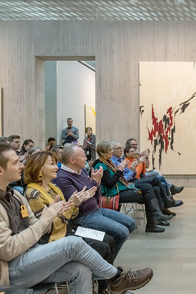 People seated in an art gallery clap at a performance