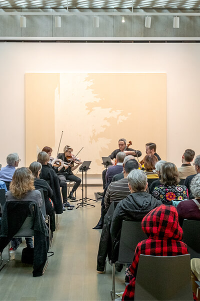People seated in an art gallery watch a string quartet perform