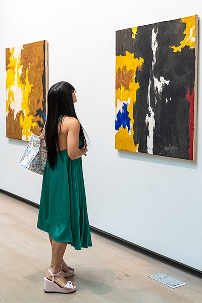 Woman wearing a green dress looks up at an abstract painting on the wall