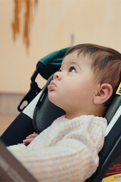 Baby leans back in a stroller and looks up with a painting behind her