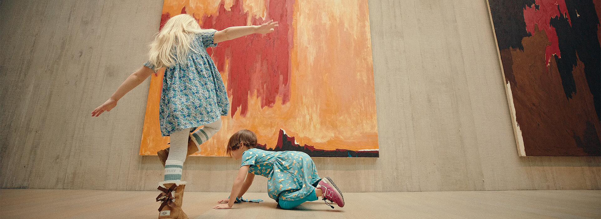 Two girls play in front of a large orange and red abstract painting