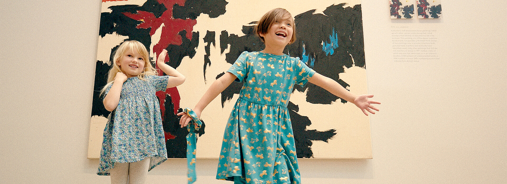 Two girls make silly poses in front of an abstract black, white, red, and blue painting