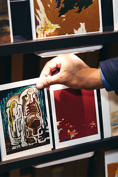 A closeup of a hand reaching down to grab a postcard with abstract art on it on a rack of postcards