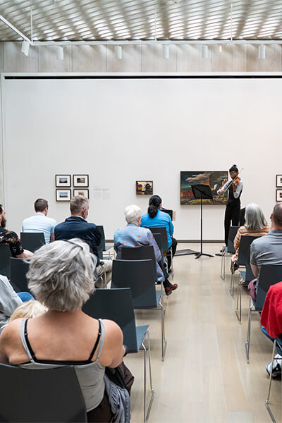 People sit and listen to chamber music in an art gallery