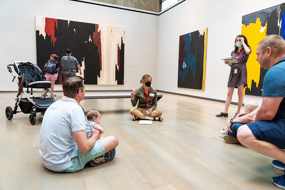 A group of caregivers and educators sit in a circle on the floor of an art gallery with their babies