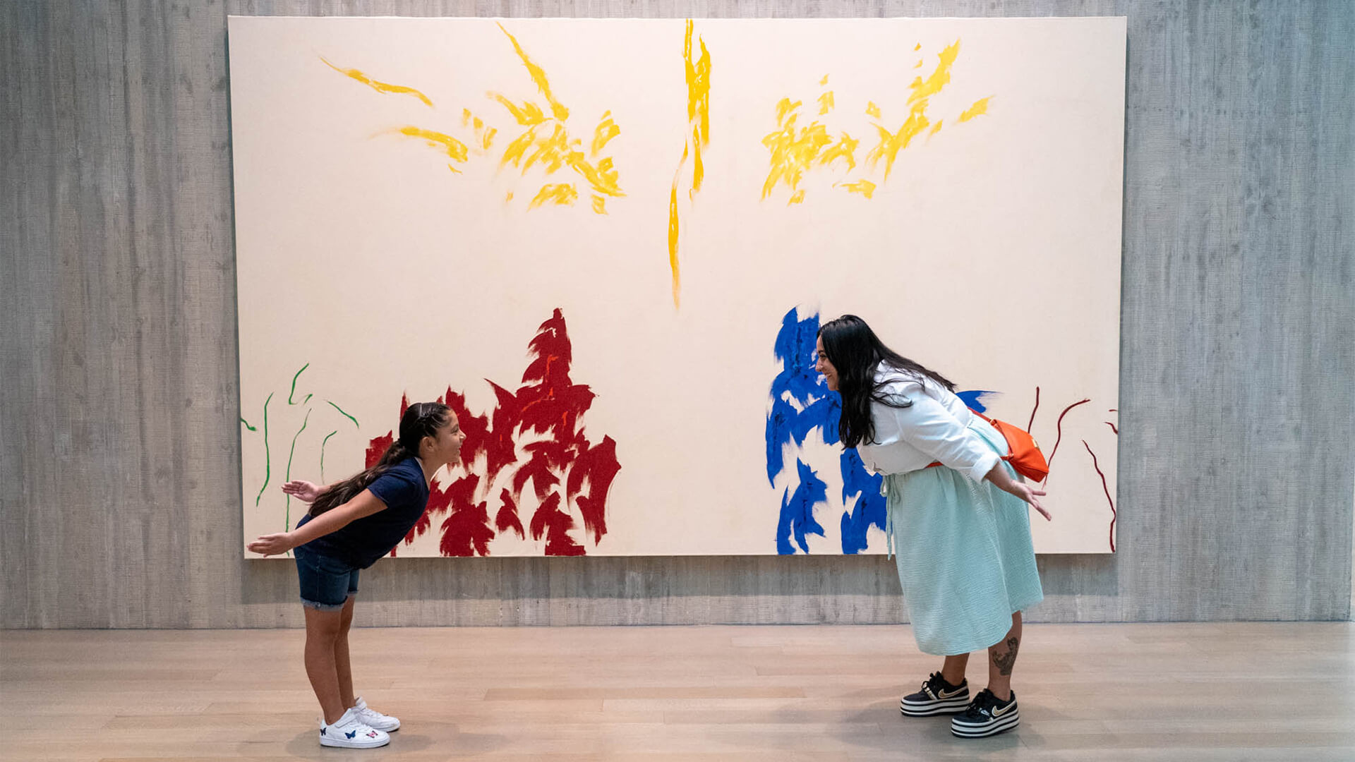A girl and her aunt lean in to make shapes in front of an abstract painting
