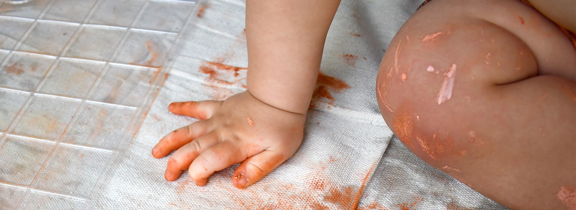 A baby sets its hand down with clay on it