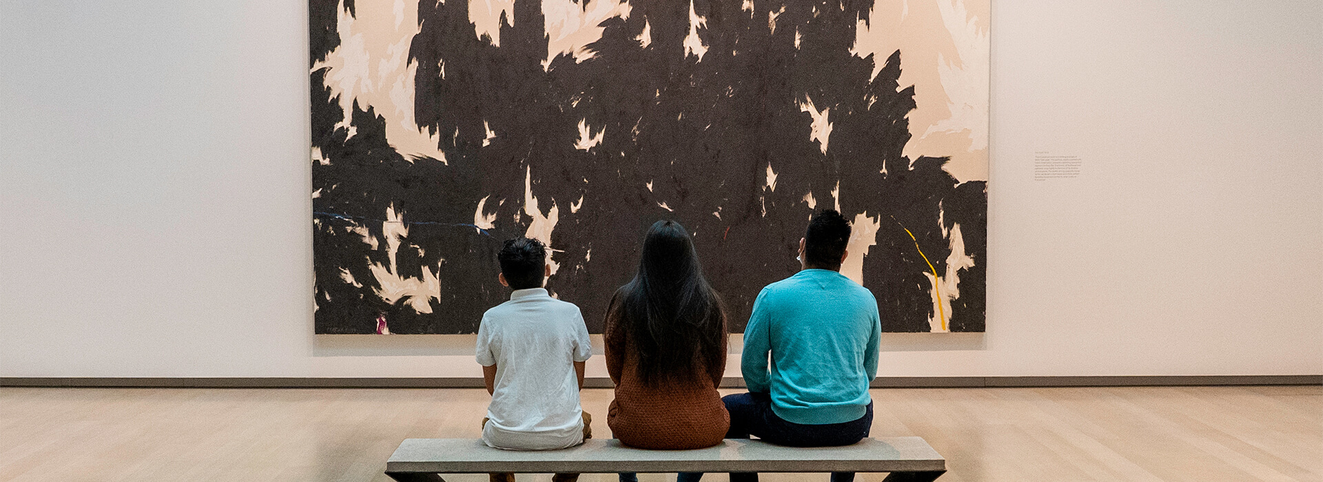 A family sits on a bench and looks at a large black and white abstract painting