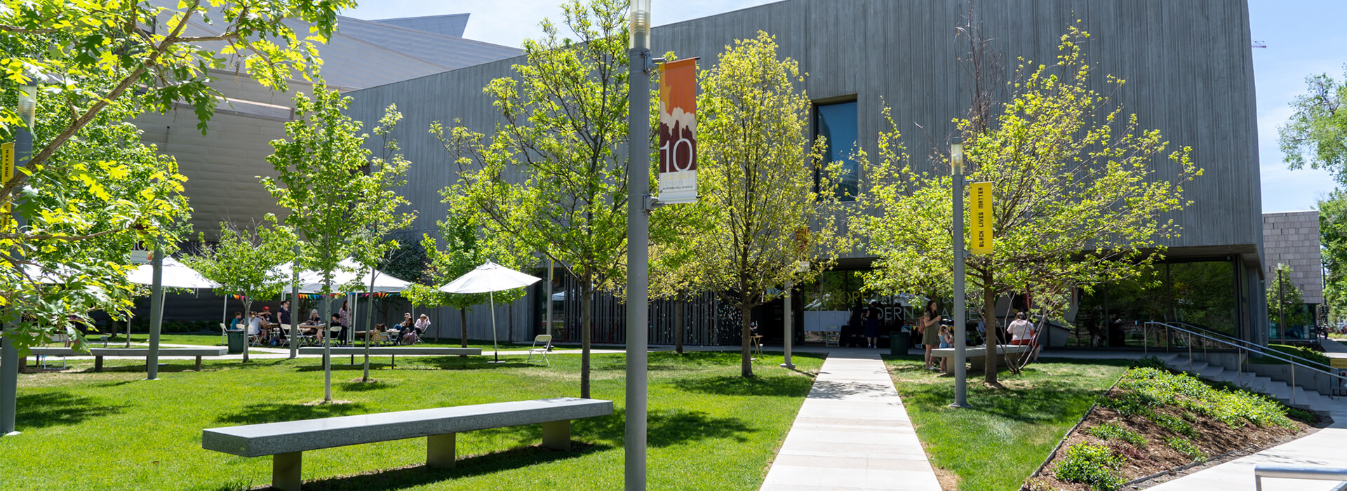 Photo of a sidewalk path in front of the Clyfford Still Museum with green grass and trees