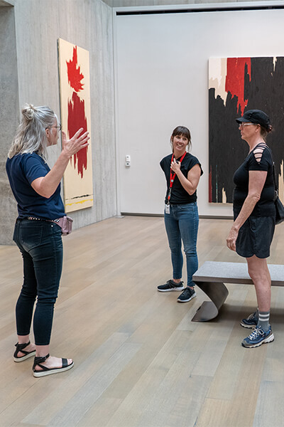 A group of teachers stand in a gallery while one holds her hands up to demonstrate how big something is