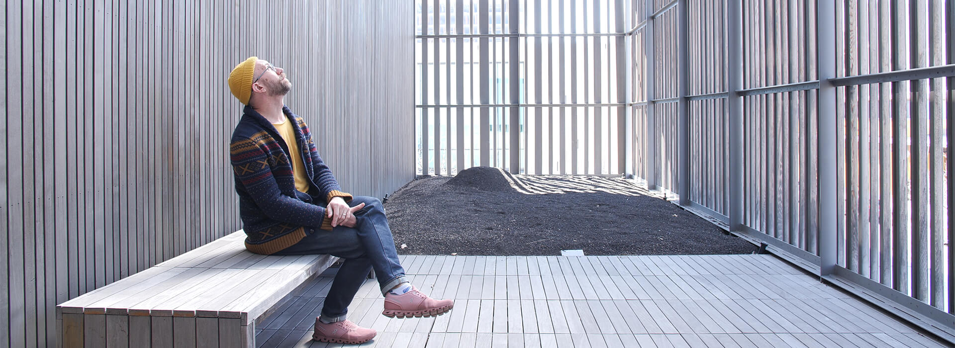 A man sits on a bench on an outdoor terrace and looks up