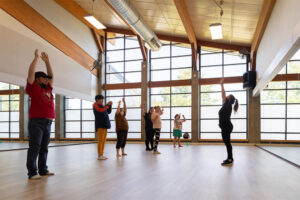 People stand in dance studio with their arms stretched up towards the ceiling