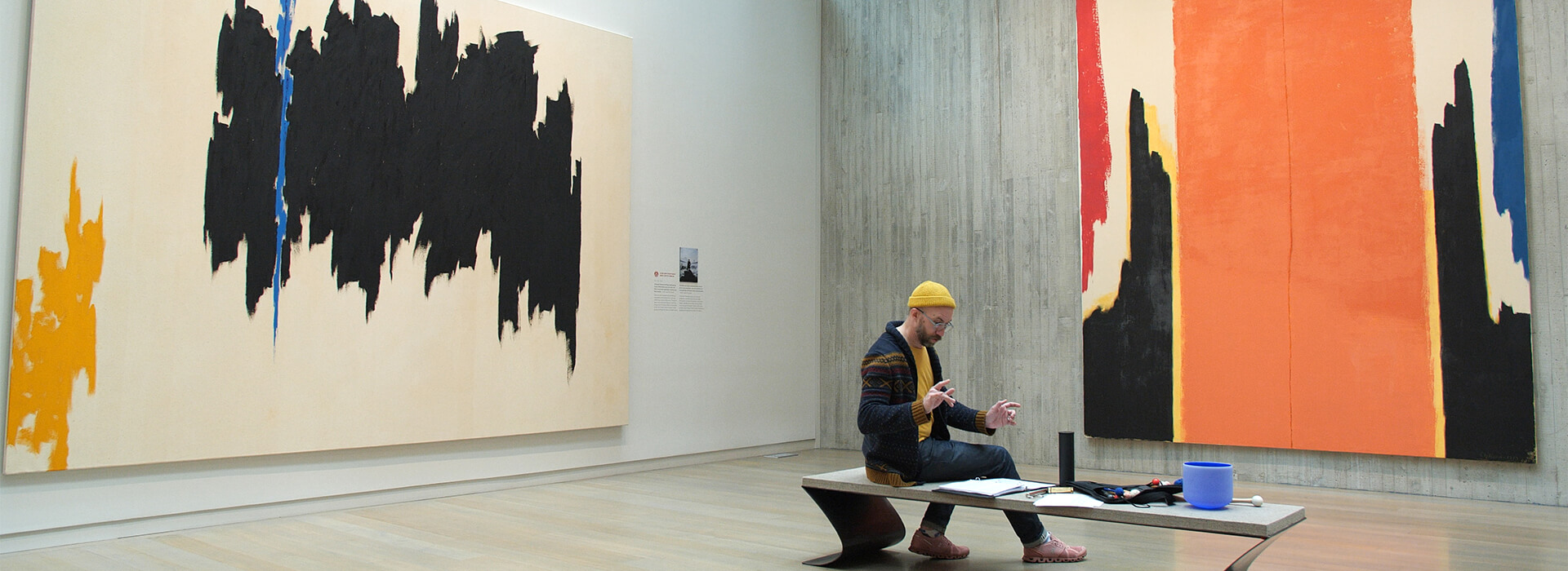 A man sits on a bench with musical equipment in an art gallery