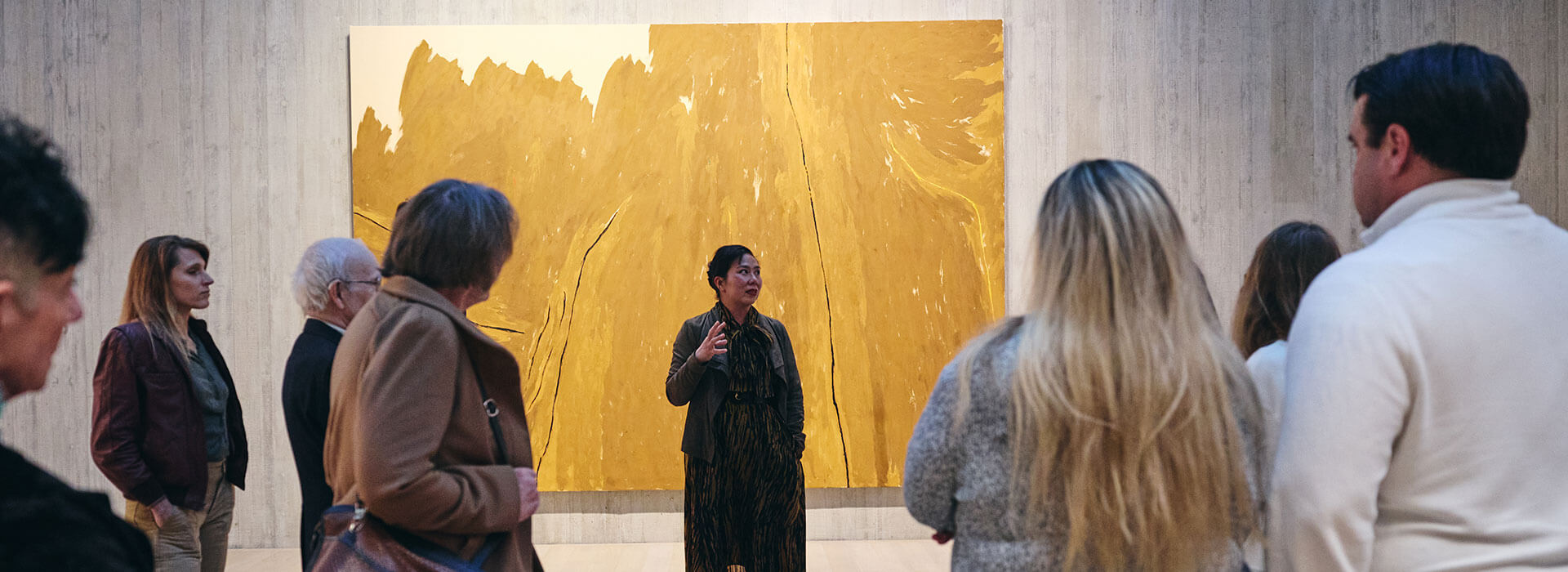 A woman gives a tour in an art gallery to a large group of adults