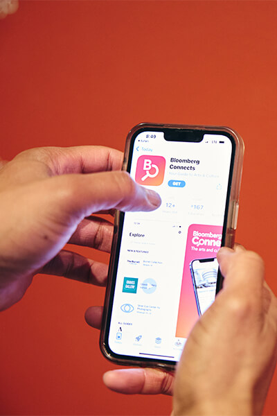 A person holds up a phone with a screen that has the Bloomberg Connects app ready to download