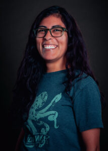 A woman wearing glasses and a t-shirt with an image screenprinted smiles at the camera