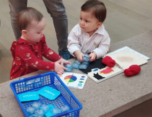Two babies play with ice cubes and art