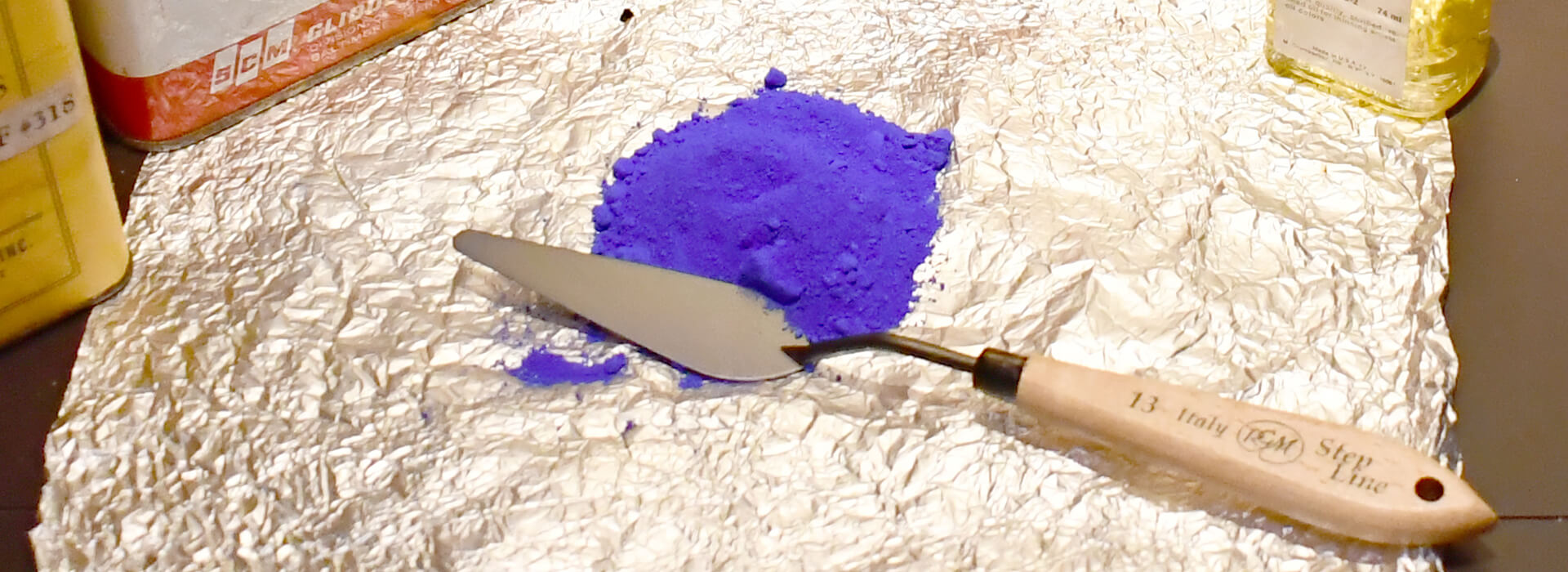 Closeup of a palette knife on aluminum foil with powdered blue pigment next to it