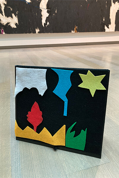 A black felt board has colorful felt shapes on it in an art gallery