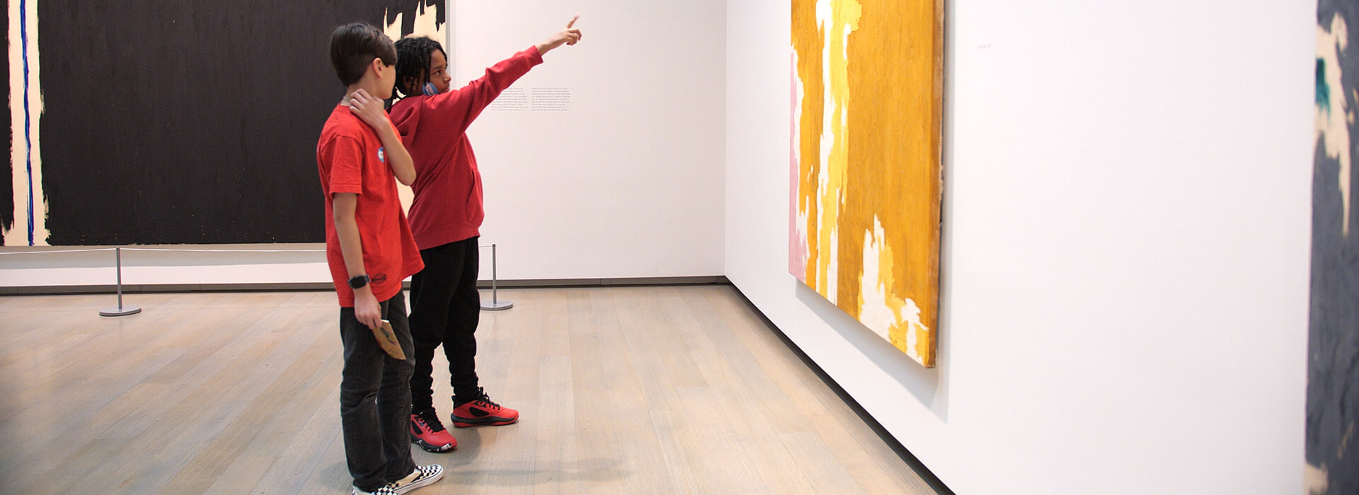 Two students look at a painting on a wall while one points at it