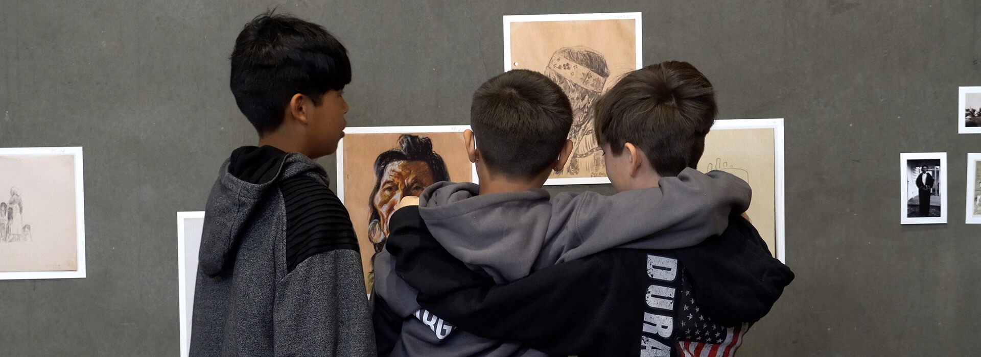 Three boys look at artworks together